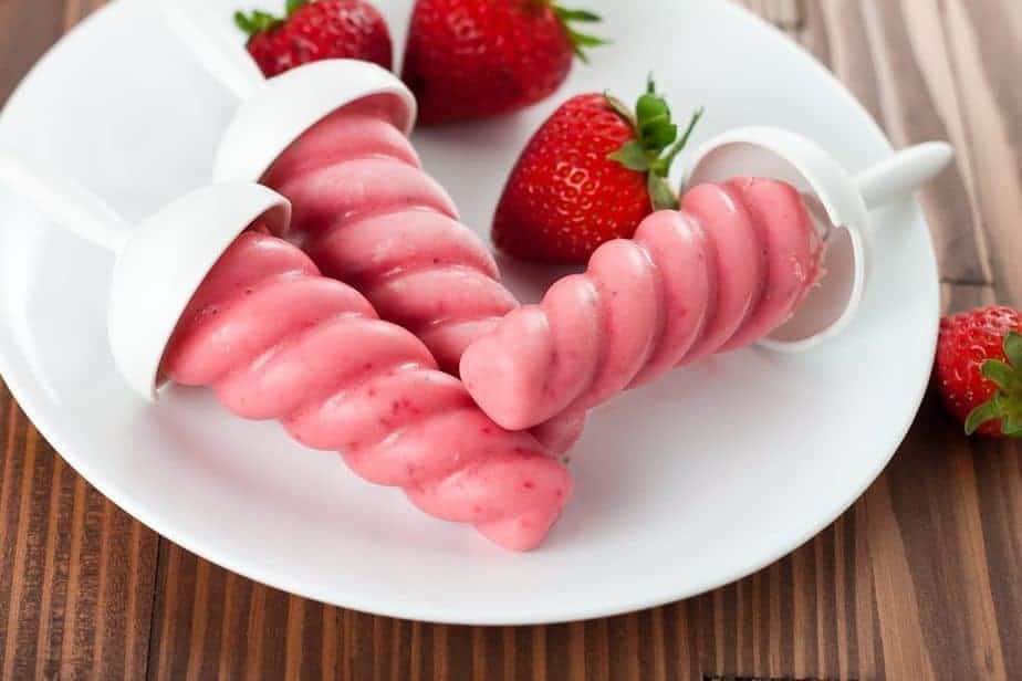 Three strawberry popsicles and strawberries in a white plate. These Healthy Strawberry Greek Yogurt Popsicles are a healthy and refreshing frozen treat that everyone will look forward to on a hot summer day.