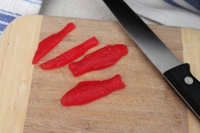 A slice of Swedish Fish in a cutting board with a knife.