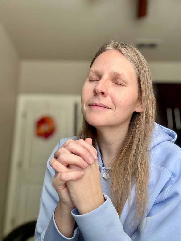 Woman with hands folded in prayer and eyes closed, slightly smiling as she prays