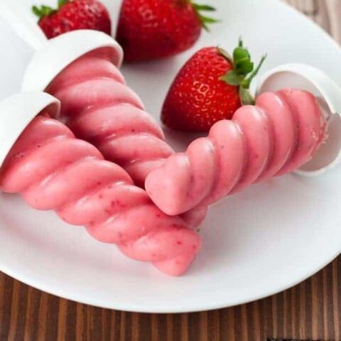 Three strawberry popsicles and strawberries in a white plate. These Healthy Strawberry Greek Yogurt Popsicles are a healthy and refreshing frozen treat that everyone will look forward to on a hot summer day.
