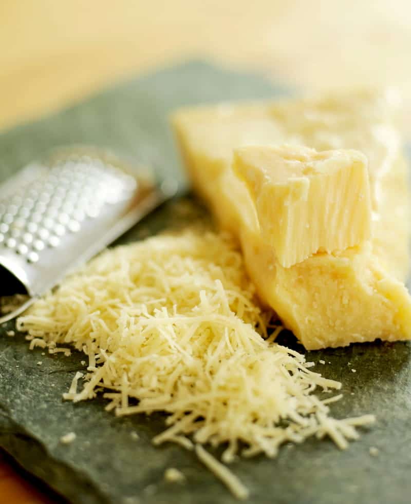 Clock of cheese partially grated with cheese grater on cutting board