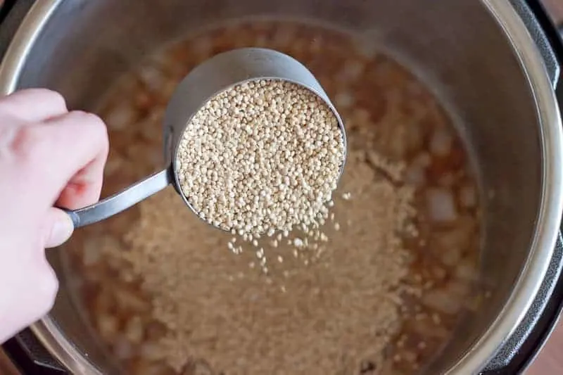 Measuring cup of quinoa being poured into a pot