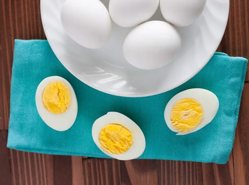 Plate of hard boiled eggs, some cut in half showing yolk on napkin