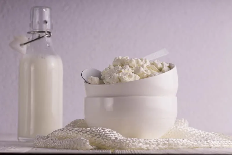 Bowl of cottage cheese next to a glass bottle of milk