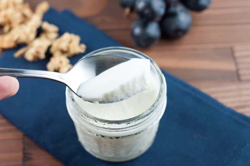 spoonful of yogurt out of mason jar with grapes and granola in background