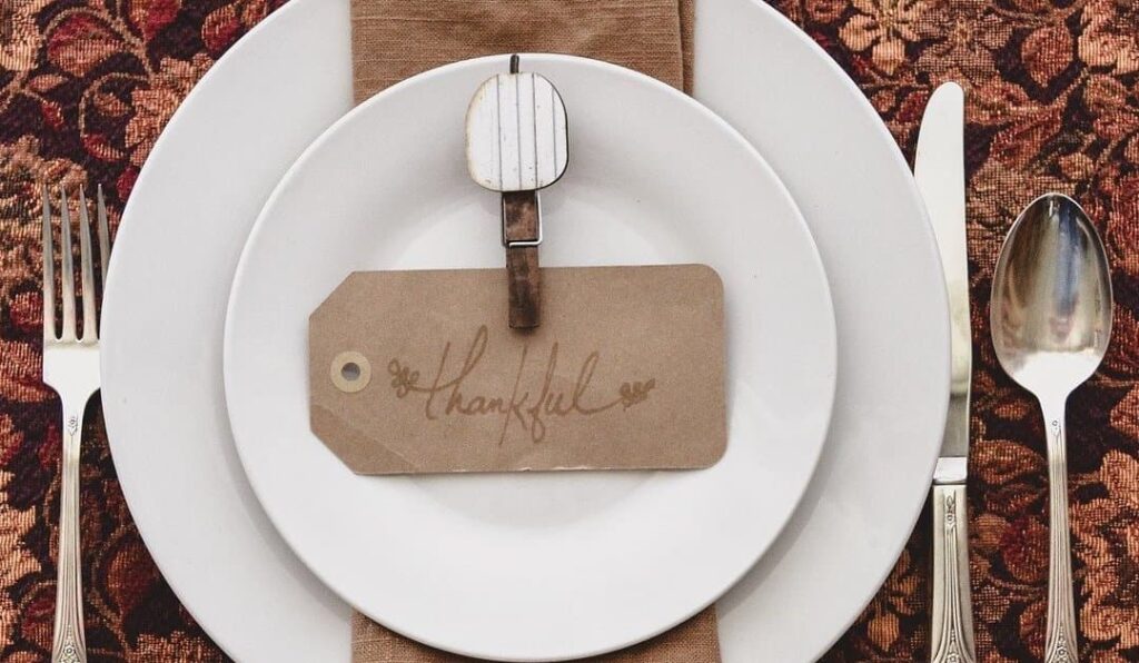 Prayers For Thanksgiving Dinner - place setting at Thanksgiving table with the words "thankful" drawn on brown tag