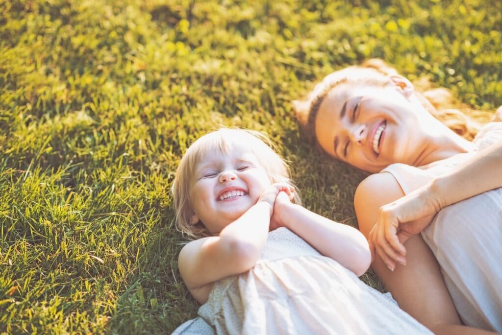Mom and child laughing together as they lay in the grass and sunshine