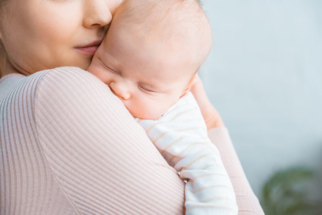 prayers for a new baby - woman holding a sleeping newborn against her cheek and up to her shoulder