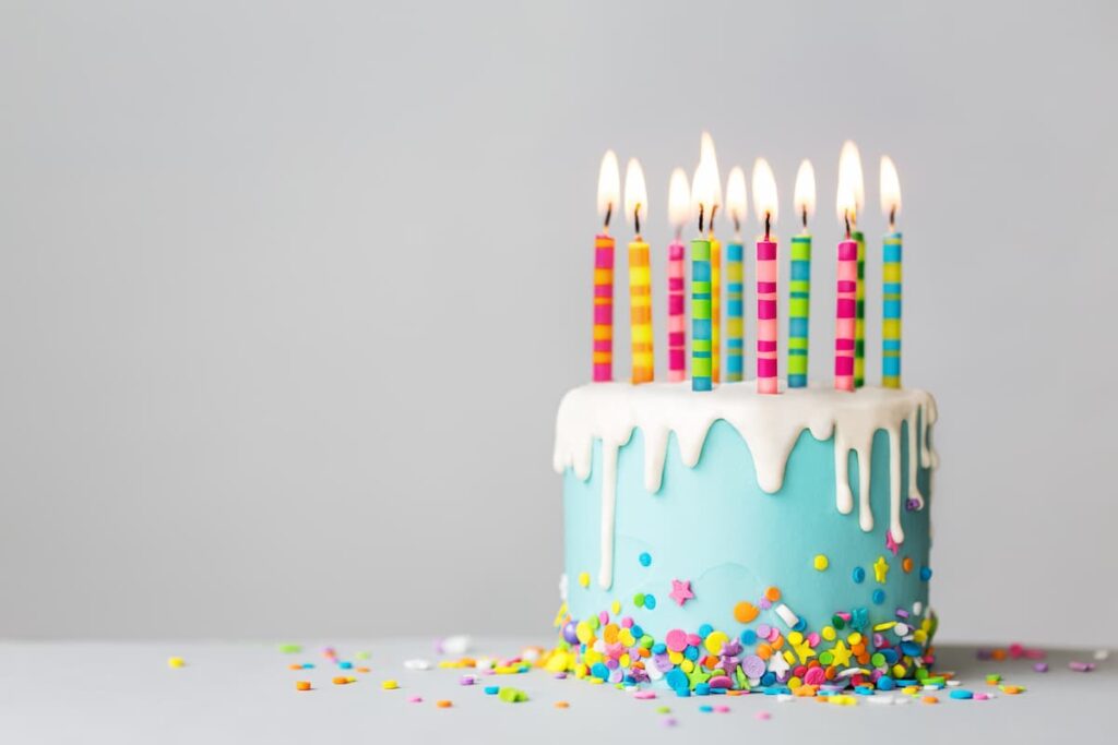 Birthday Prayers - teal birthday cake with lit candles set on a table with confetti
