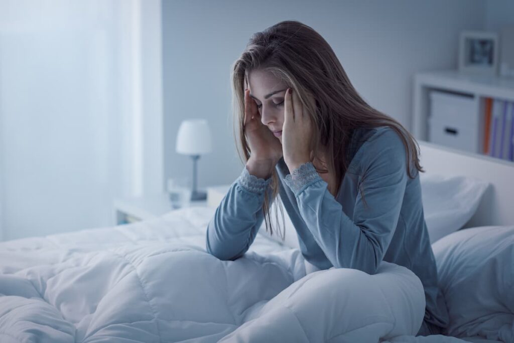Prayers For Insomnia Relief - woman sitting up in bed with hands to her head in frustration
