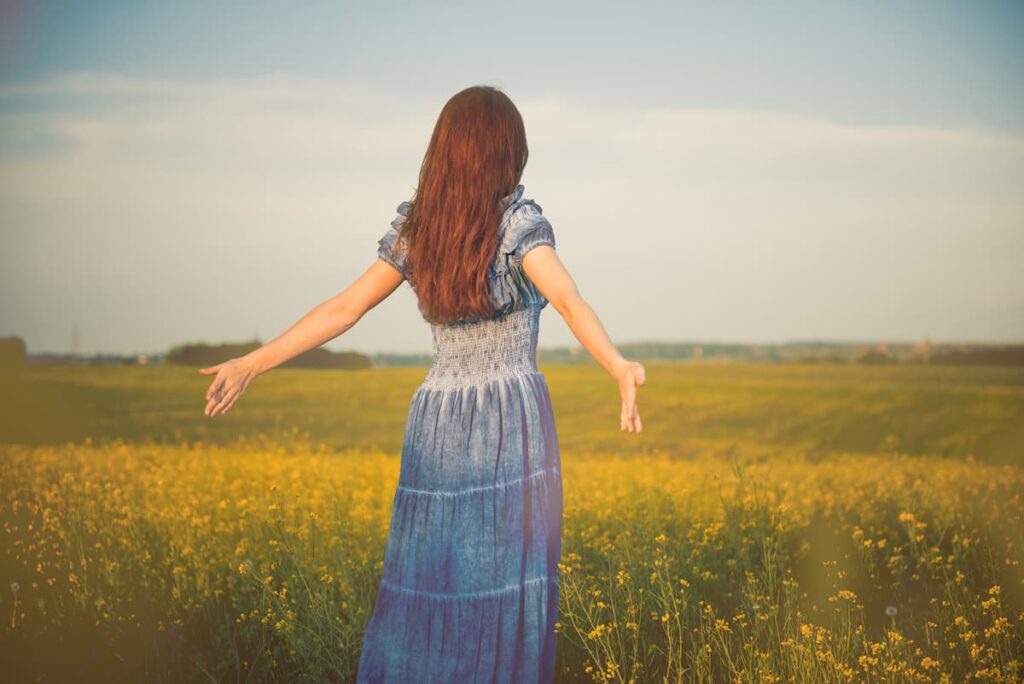 Prayers For Joy - woman in blue dress standing in field with arms outstretched