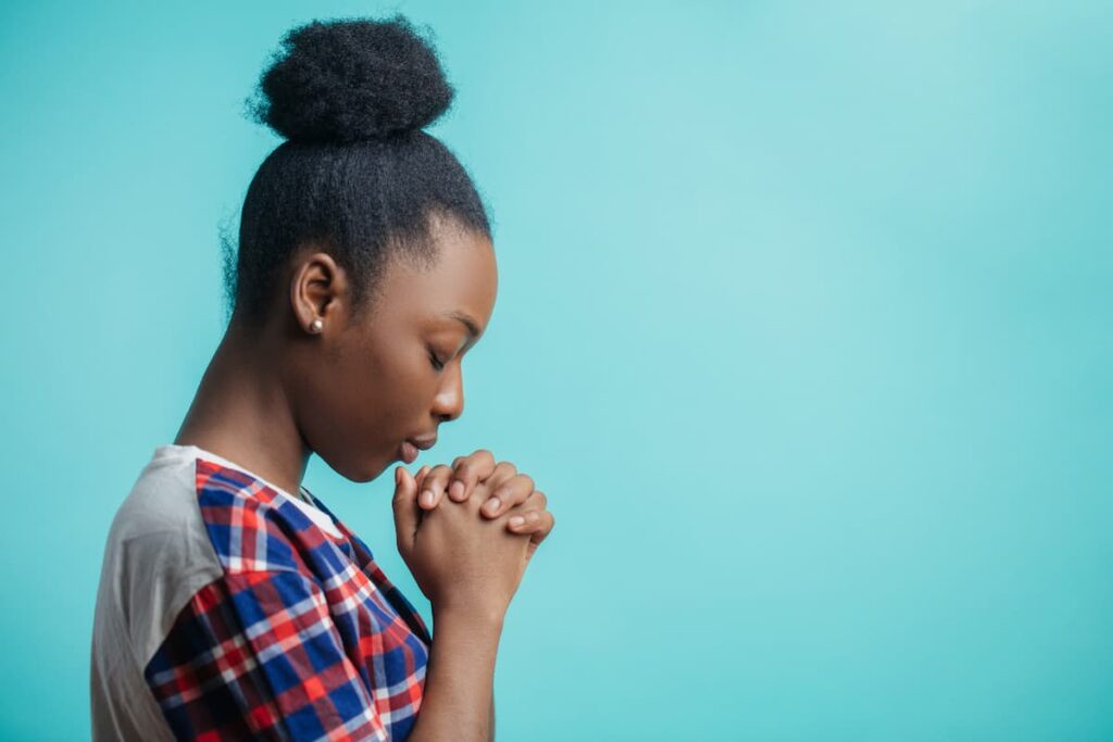 Prayers For Self Control - woman bowing her head in prayer wearing a plaid shirt in front of a teal background