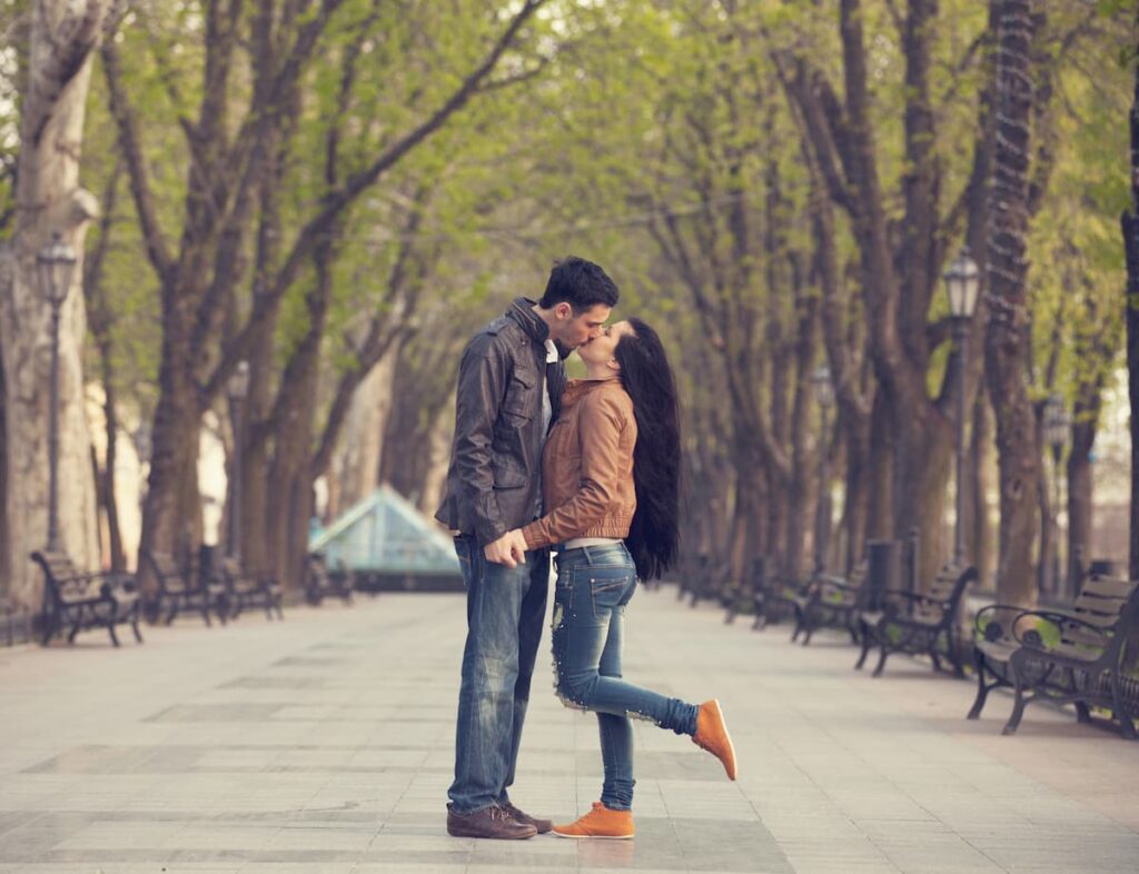 Prayers For Your Boyfriend - Man kissing a woman popping her leg up behind her in a line of trees