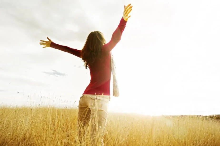Bible Verses on Freedom - woman standing in field with her arms in the air looking toward the sky