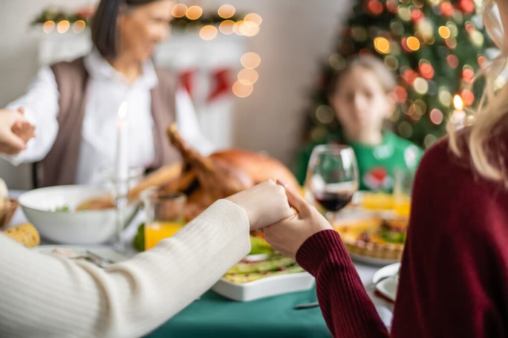 Prayers for the Christmas Season - family holding hands around Christmas dinner table with tree in the background