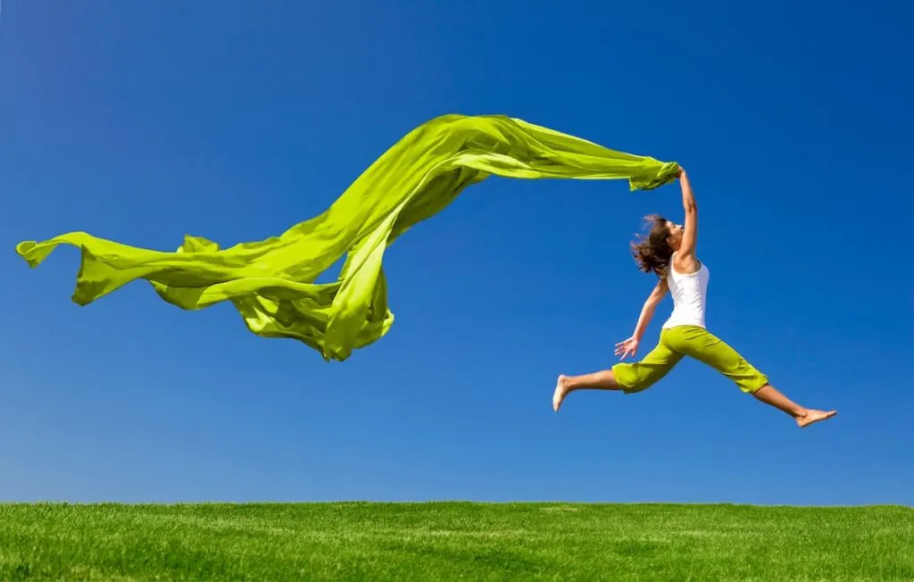 Bible Verses on Health - healthy woman jumping across grass holding long bright green fabric behind her