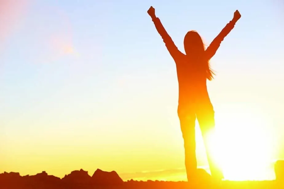 Bible Verses on Overcoming - woman standing against sunset with arms raised overhead in victory