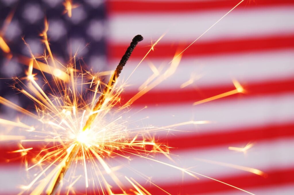 Prayers For The 4th Of July - lit sparkler sparking in front of the American flag