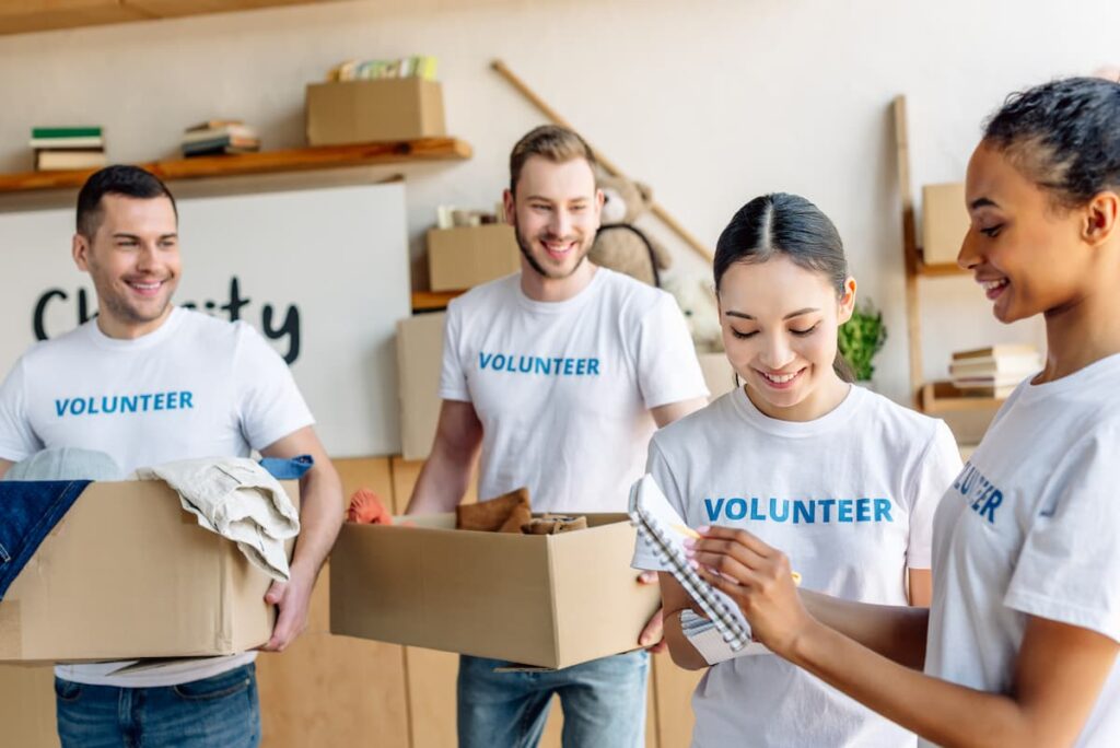 Prayers For Volunteers - 4 young volunteers in t-shirts carrying boxes