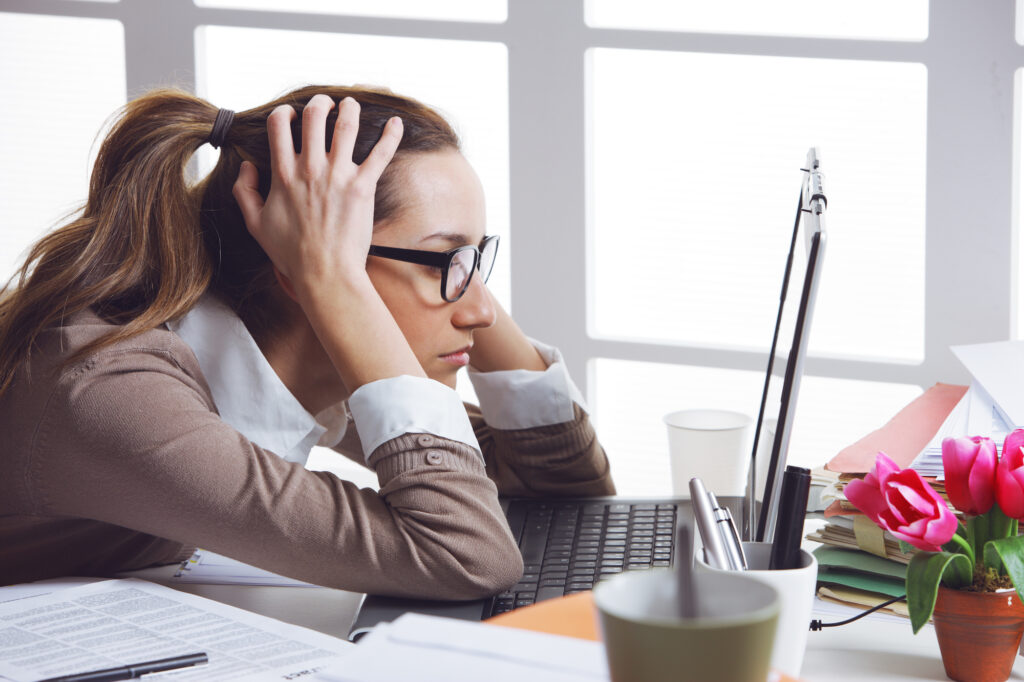 Woman sitting at her desk in front of her computer screen hands holding her head looking stressed out