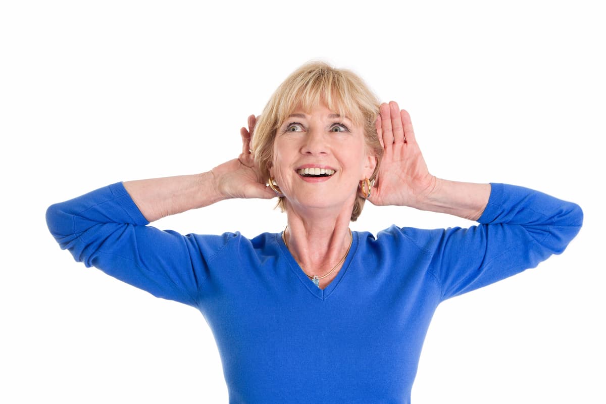 4 Ways God Speaks To Us - Woman in blue shirt cupping hands behind ears looking up and listening