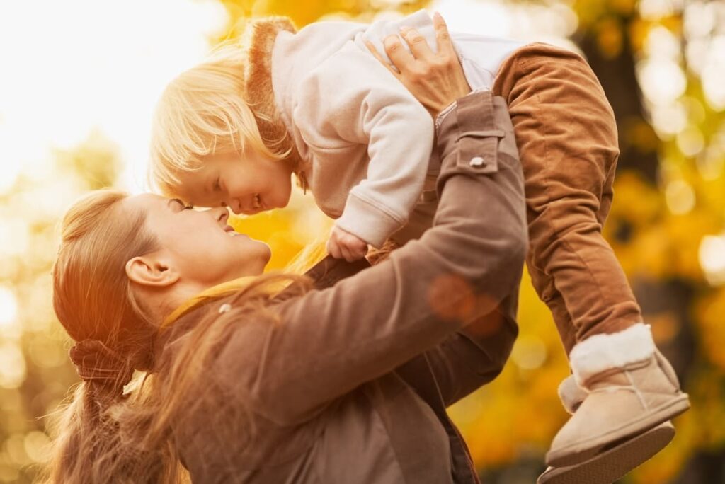 Mom holding her young child up in her arms and nuzzling them close
