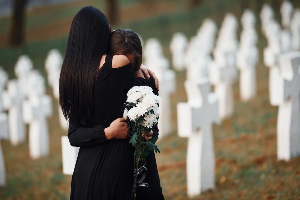 two women dressed in black hugging each other at a cemetery, grieving.
