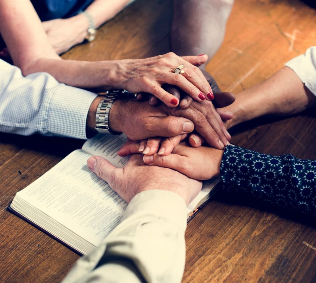 Group of hands stacked on each other on top of a bible praying.