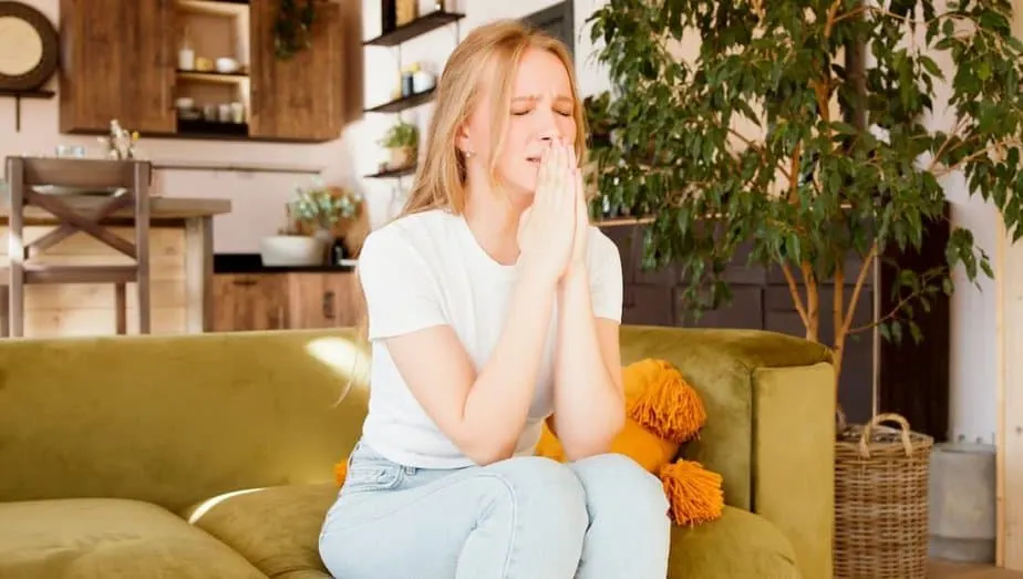 Young woman sitting on a couch eyes closed hands folded in prayer