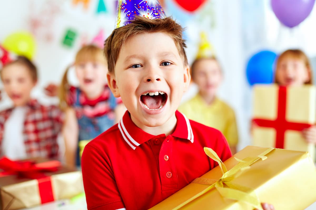 Excited young boy at his birthday party with friends - holding a gold wrapped gift box