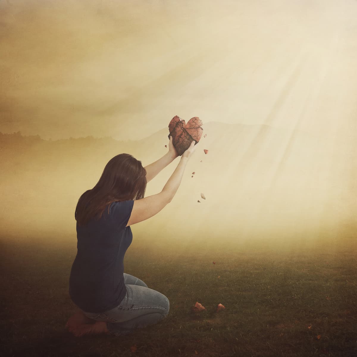 woman on her knees holding up a broken heart to the sky seemingly in prayer