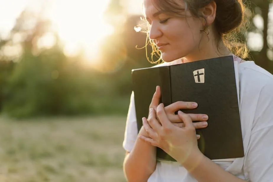 woman eyes closed holding an open bible to her chest smiling