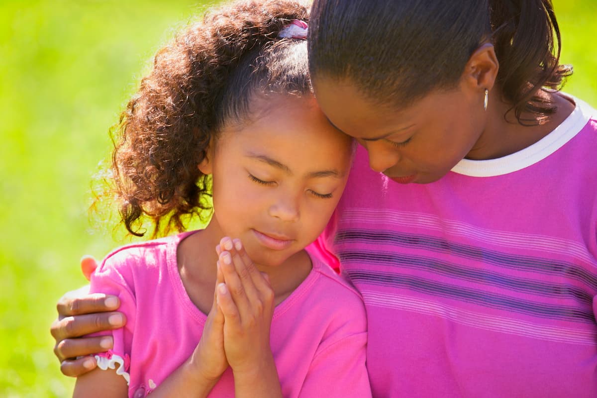 Woman embracing her daughter who has praying hands
