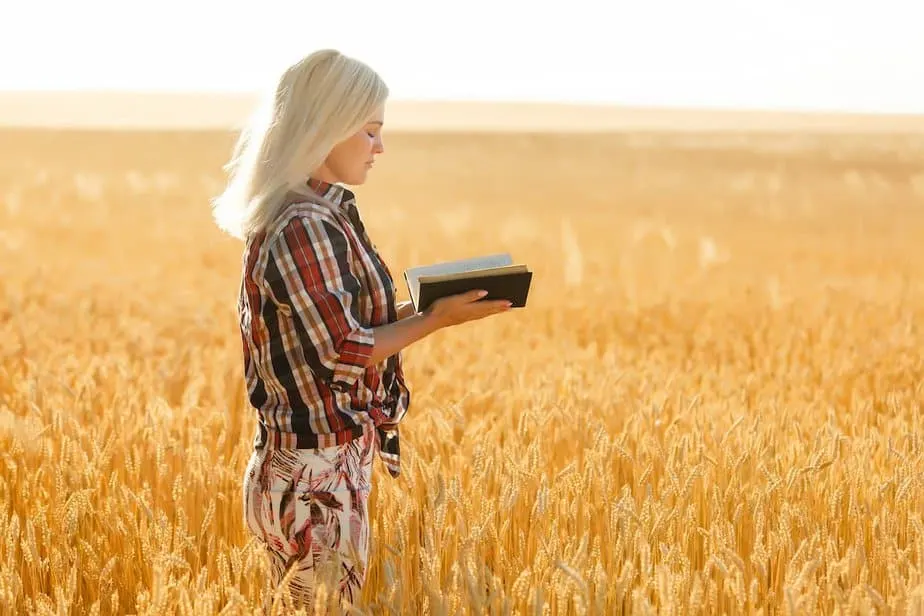 Woman holding a Bible standing in the middle of a wheat field for Verses About Harvest
