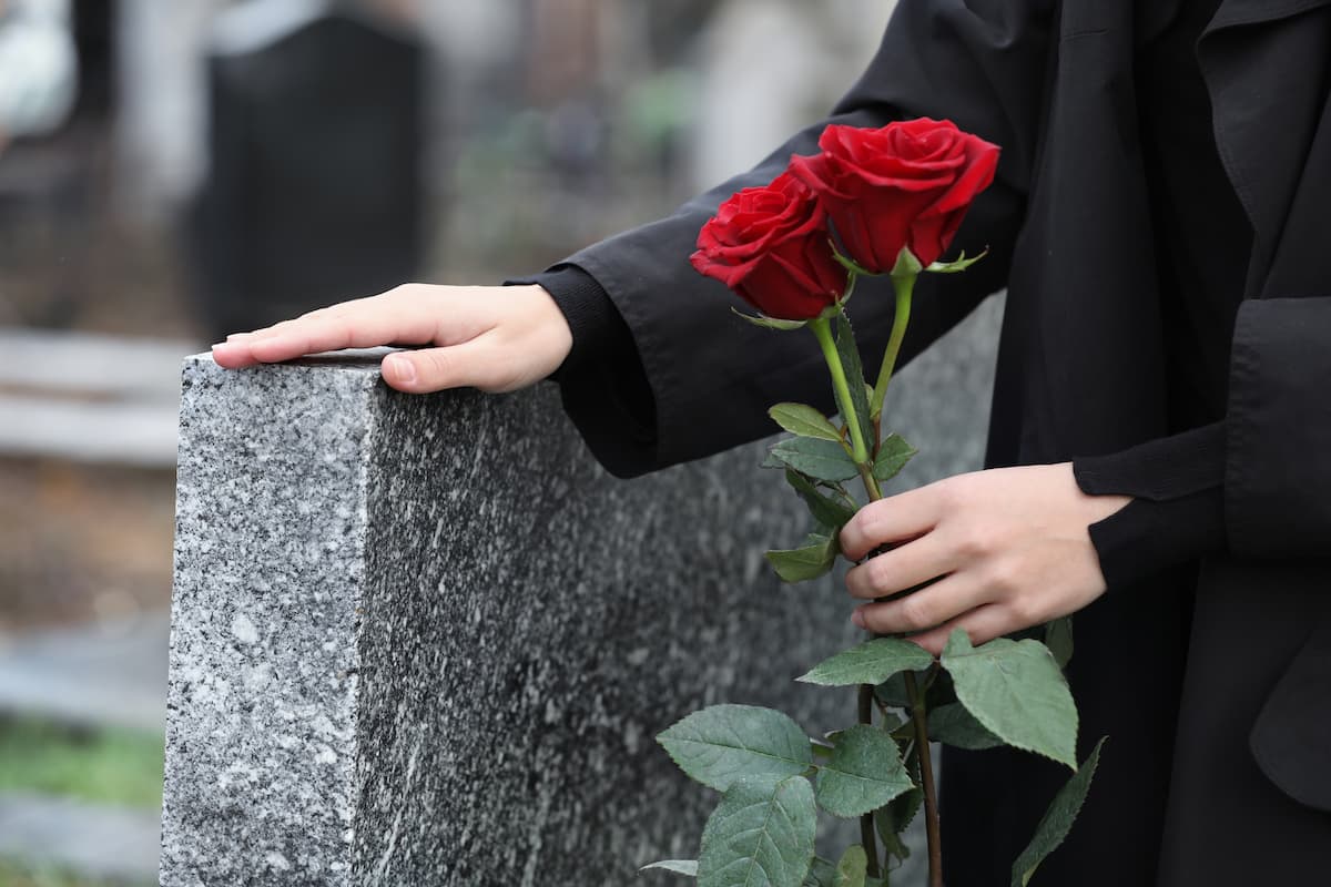 Woman holding 2 roses with a hand on a gravestone - 3 prayers to comfort a grieving friend