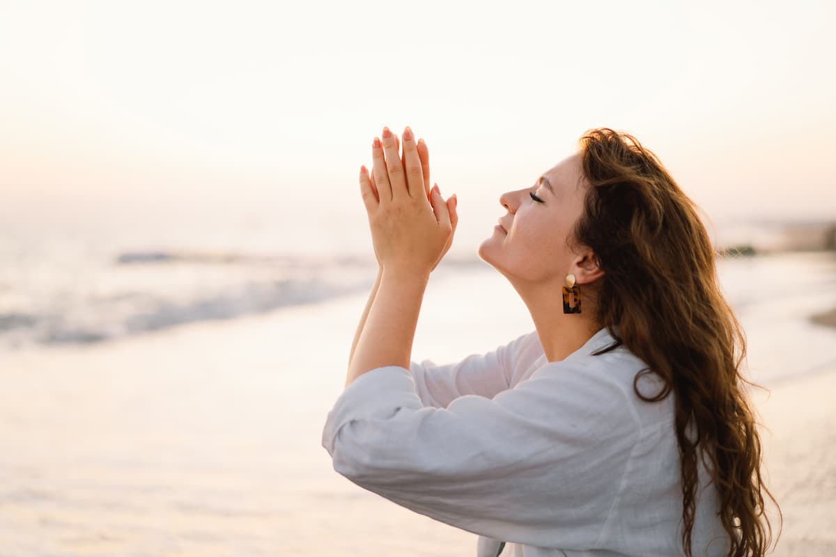 Woman at the beach with folded hands praying - 4 prayers for peace of mind