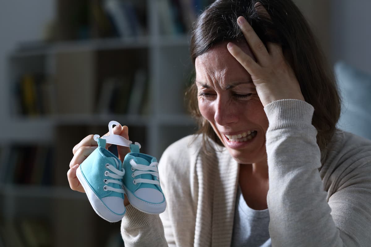 Woman crying and grieving while holding a pair of blue baby sneakers for 11 prayers for a mother who lost her son