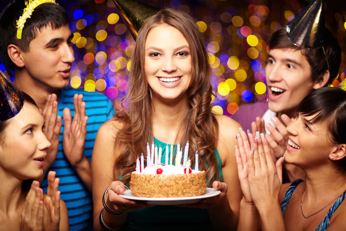 Woman holding a birthday cake surrounded by friends wearing party hats for 25 birthday prayers for myself