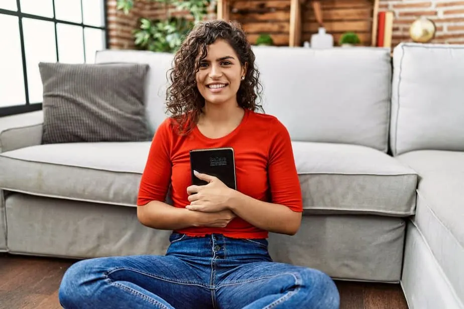 Woman in red shirt sitting cross-legged on the floor holding a bible for 13 empowering bible verses for women