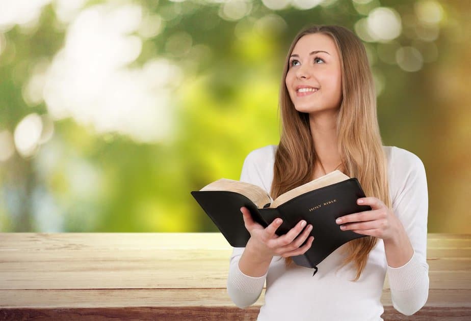 smiling young woman looking up and holding an open bible for 35 Bible verses about favor 
