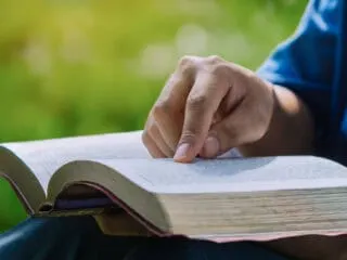 Leader or pastor sitting outdoors with their hand on the Bible