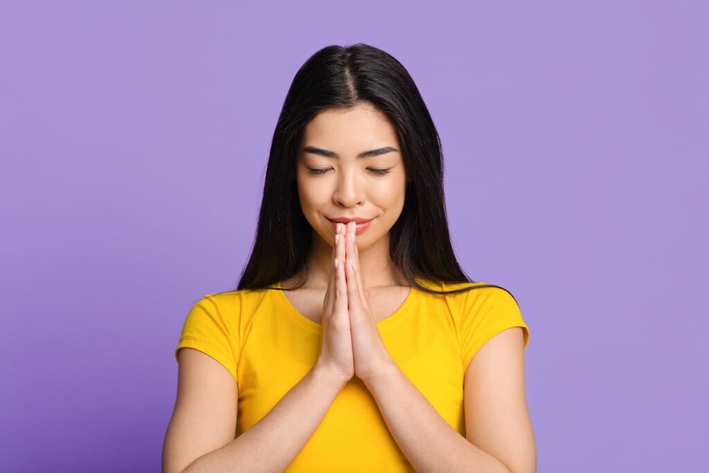 Prayers to increase faith - Calm asian girl praying with hands clasped near face and eyes