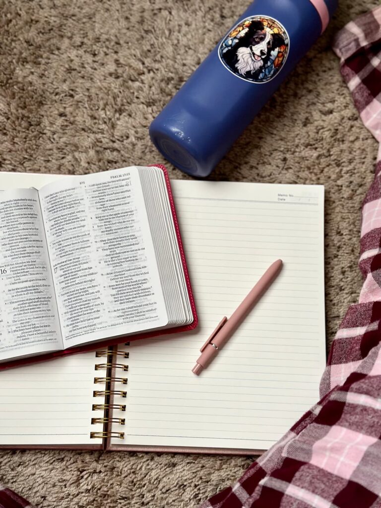 Open journal with a pink pen, open Bible, and a water bottle laying on the floor