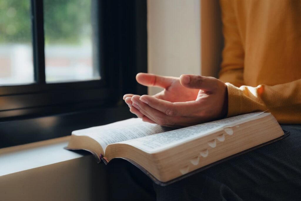 woman sitting next to a window with a Bible on her lap and her hands open