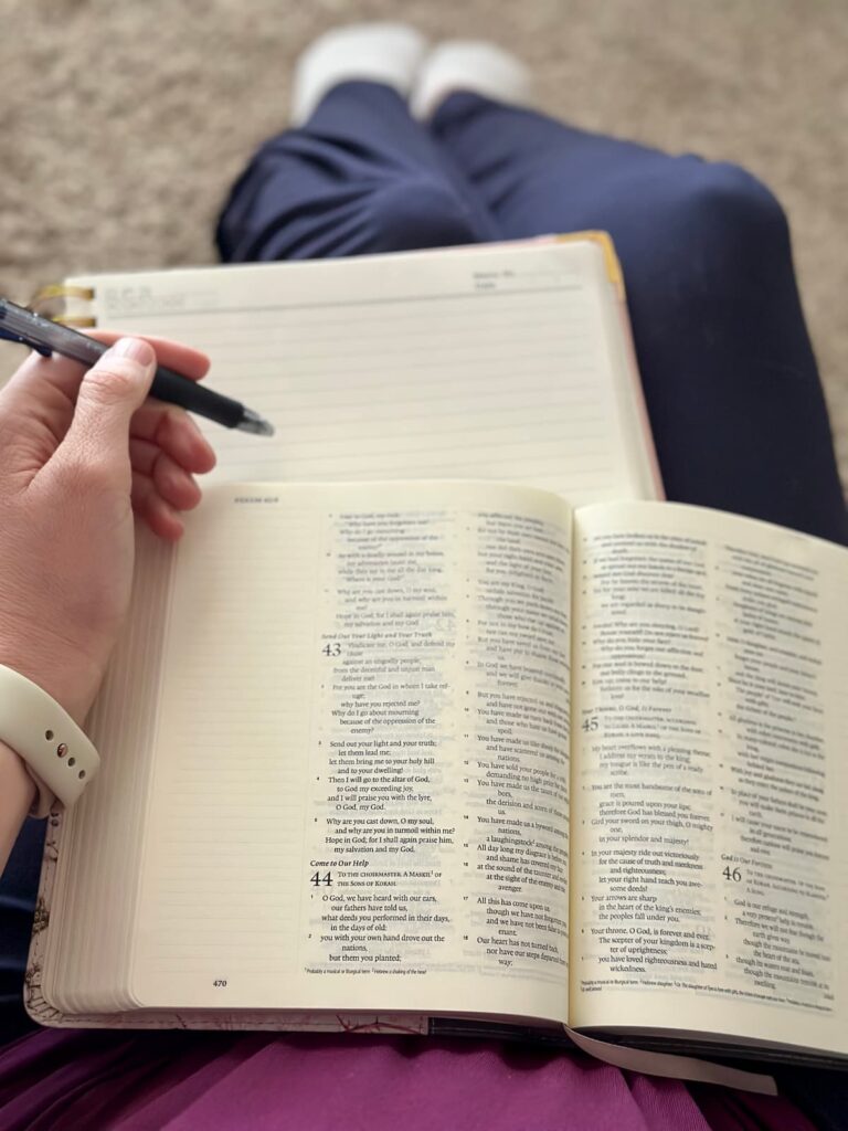 Open Bible with a blank journal page and a pen in a hand, sitting on bent legs sitting on the floor