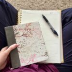 Overhead picture of crossed legs with a flowery Bible, journal, and pen in a woman's lap.