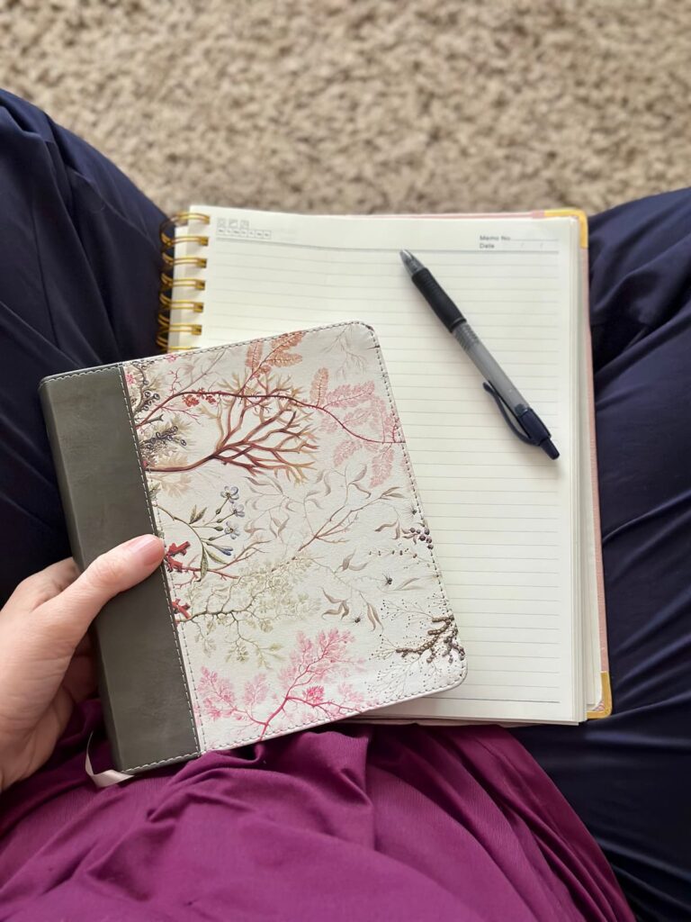 Overhead picture of crossed legs with a flowery Bible, journal, and pen in a woman's lap.