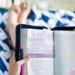 Woman lying in hammock holding Bible up