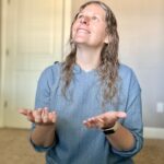Woman kneeling holding her hands out in front of her smiling and looking up towards God